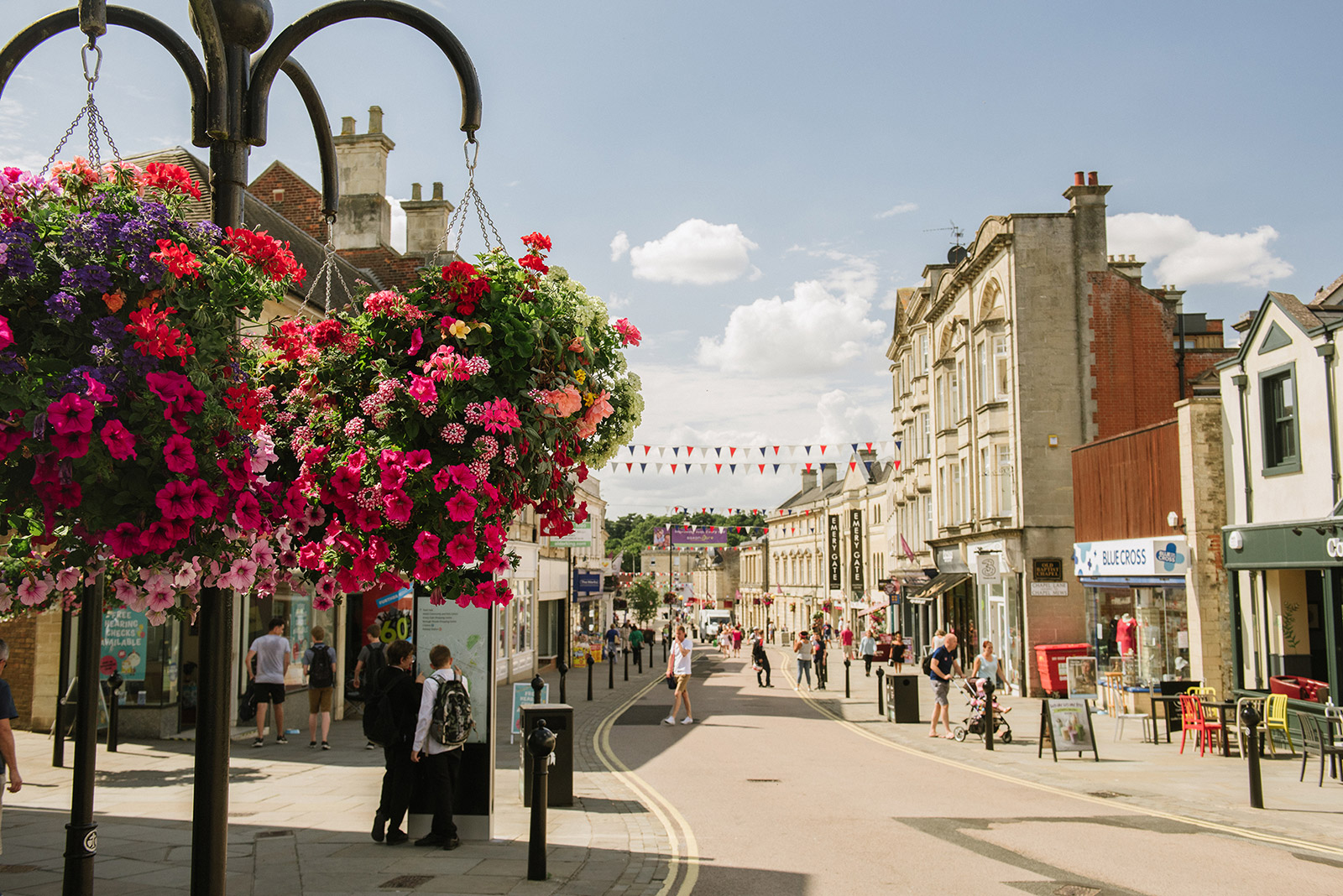 Chippenham high street on a sunny day, with colourful hanging baskets of flowers.