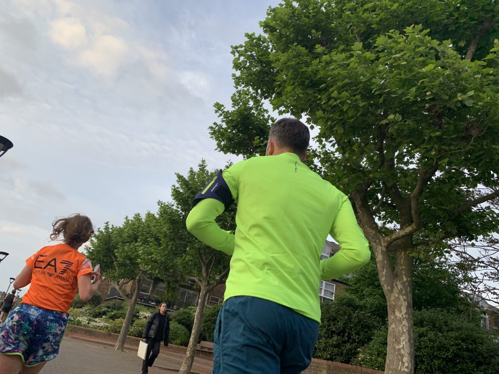 People jogging outdoors along a tree-lined path, with one person in a bright green running shirt in the foreground.